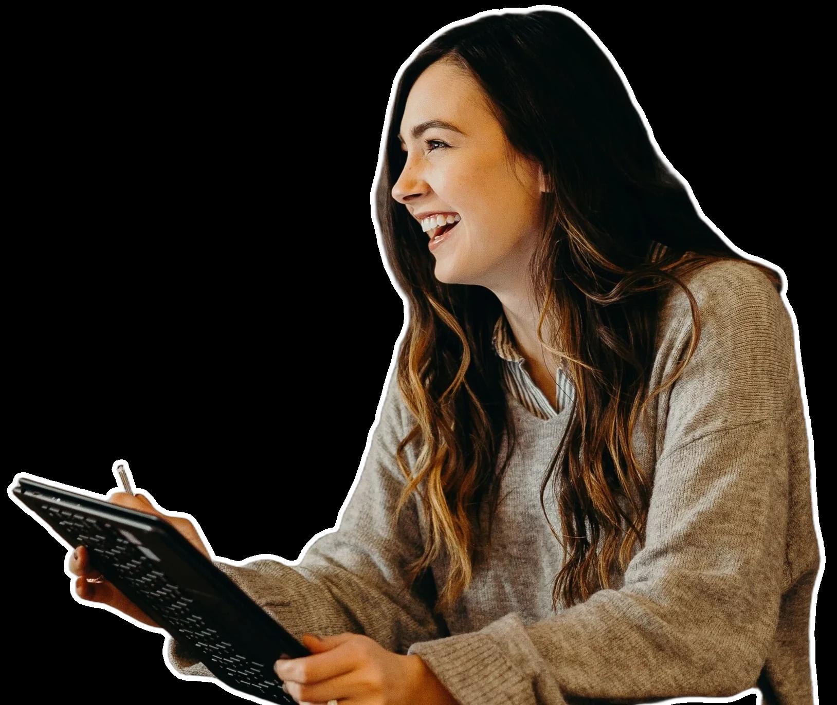 Someone with long dark hair in a grey sweater laughing, holding a tablet and stylus