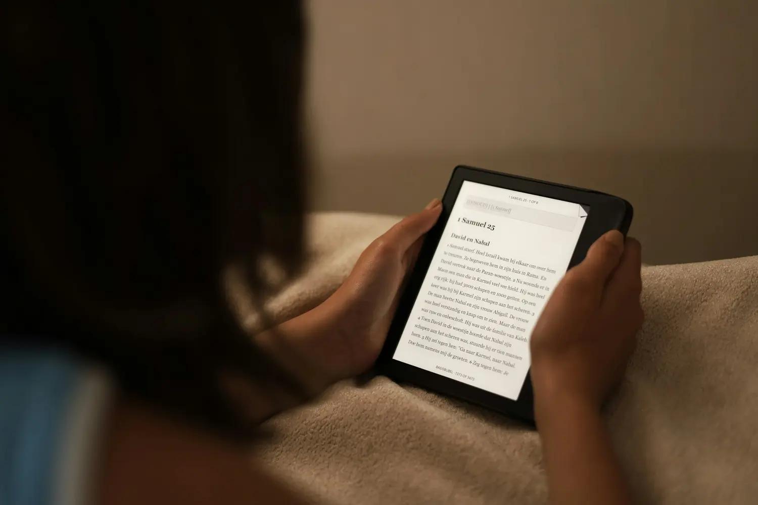 Someone curled up under a blanket reading a book on an e-reader