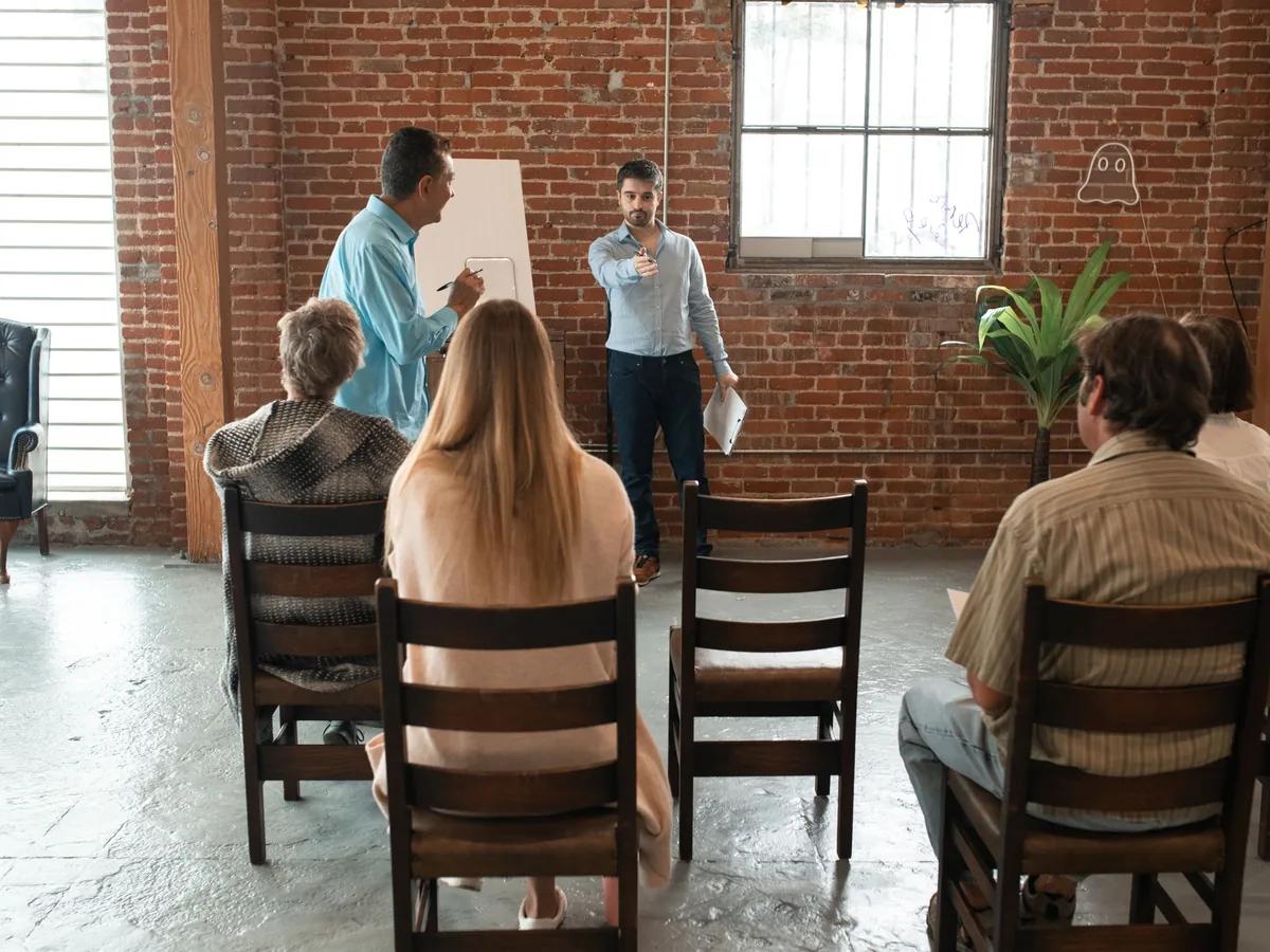 A small group seated in a brick-walled loft, watching someone present at a flip chart