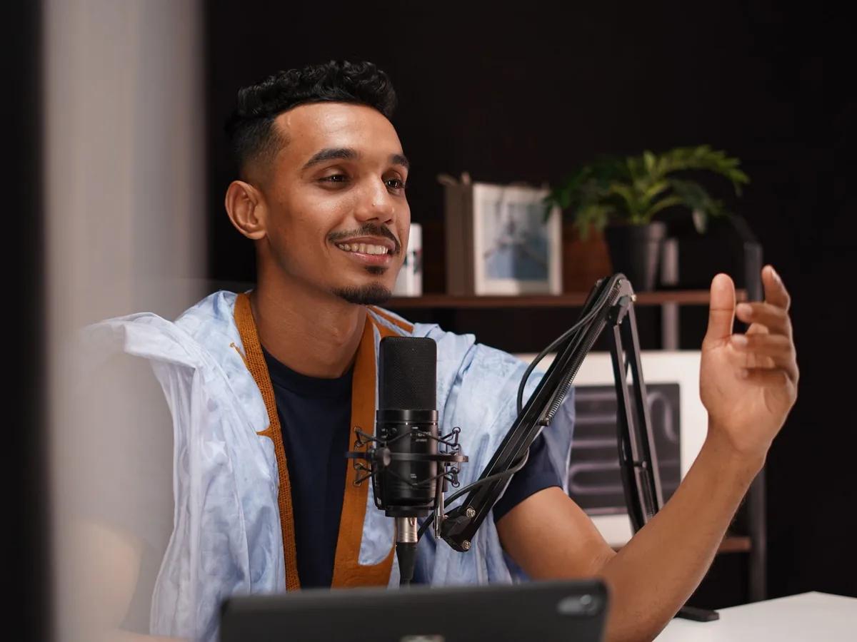 Someone talking into a studio microphone at a desk, mid-gesture